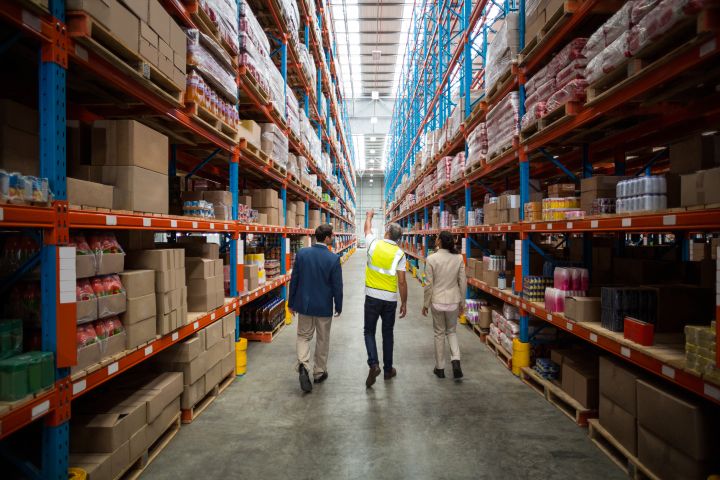 Workers walking through a tall warehouse corridor with industrial ceiling fans
