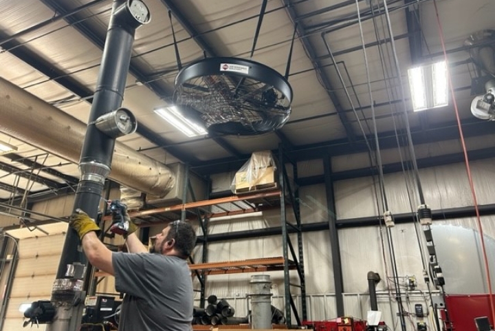 A black AirFocus fan hanging from the ceiling of a shop while a man works underneath it.